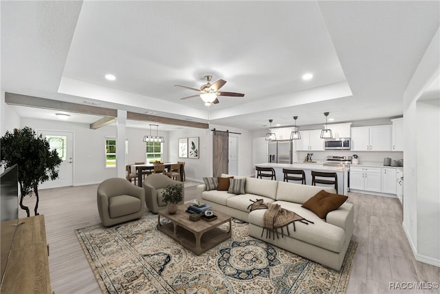 living room with a tray ceiling, a barn door, ceiling fan, and light hardwood / wood-style floors