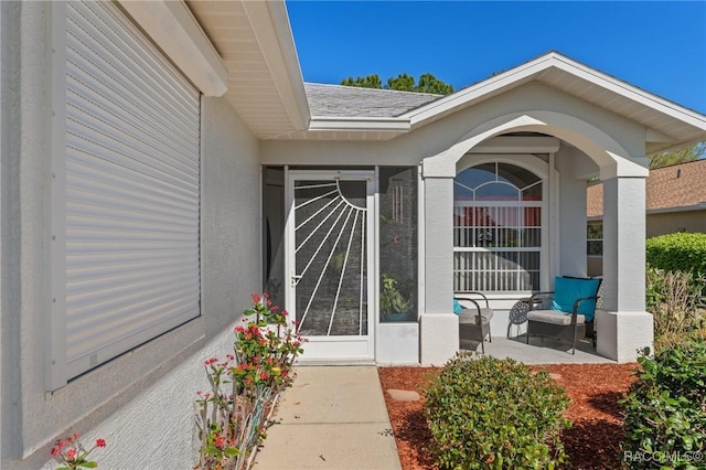 entrance to property with stucco siding, roof with shingles, and a porch