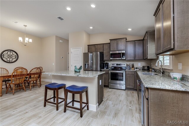 kitchen featuring sink, stainless steel appliances, vaulted ceiling, a kitchen island, and light wood-type flooring