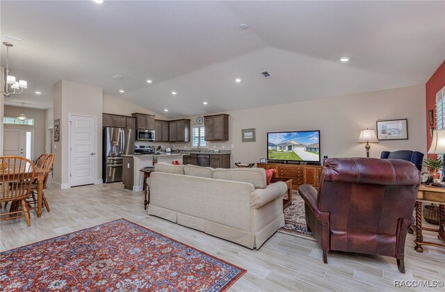 living room with a notable chandelier, lofted ceiling, and light hardwood / wood-style flooring