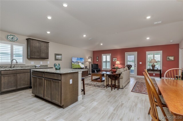 kitchen featuring light stone countertops, a kitchen bar, dark brown cabinetry, light hardwood / wood-style flooring, and a center island