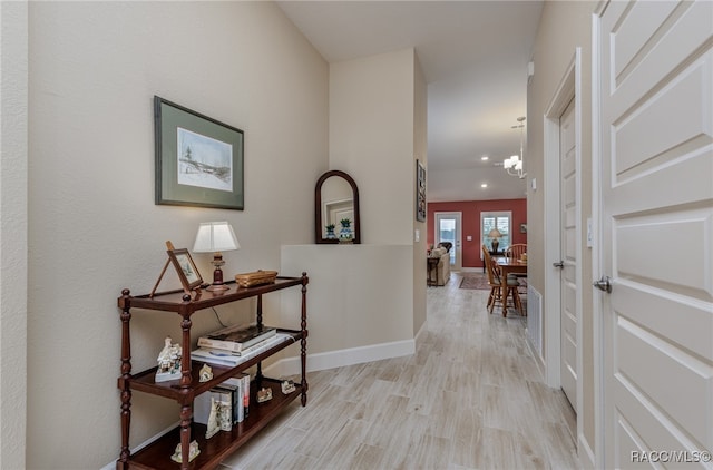 hallway with a notable chandelier and light hardwood / wood-style floors