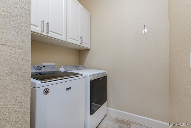 clothes washing area with cabinets, separate washer and dryer, and light hardwood / wood-style floors