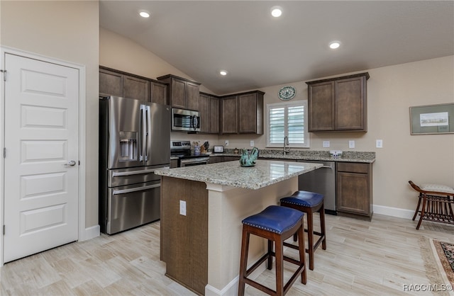 kitchen featuring light stone countertops, dark brown cabinets, stainless steel appliances, a kitchen island, and lofted ceiling