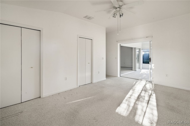 unfurnished bedroom featuring ceiling fan, vaulted ceiling, light colored carpet, and multiple closets