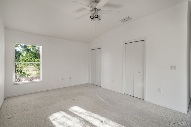 unfurnished bedroom featuring ceiling fan, two closets, light carpet, and vaulted ceiling