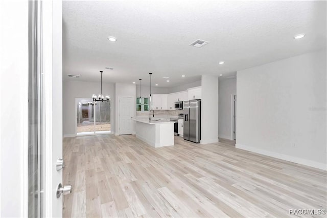 kitchen with pendant lighting, an island with sink, white cabinetry, stainless steel appliances, and light hardwood / wood-style flooring