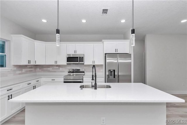 kitchen featuring appliances with stainless steel finishes, decorative light fixtures, a kitchen island with sink, and sink