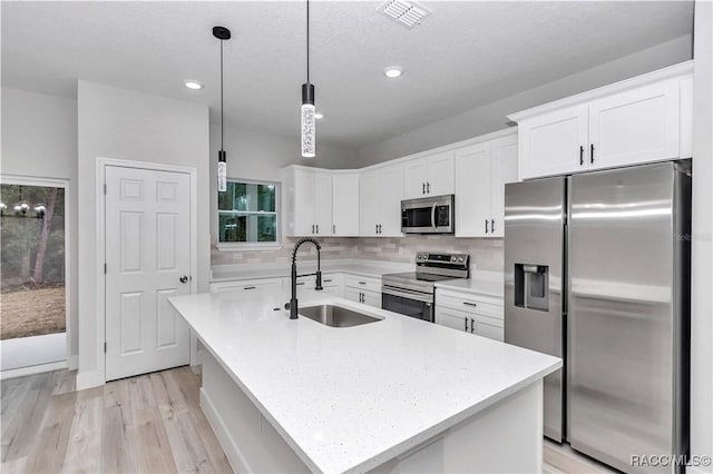 kitchen with appliances with stainless steel finishes, decorative light fixtures, an island with sink, sink, and white cabinets