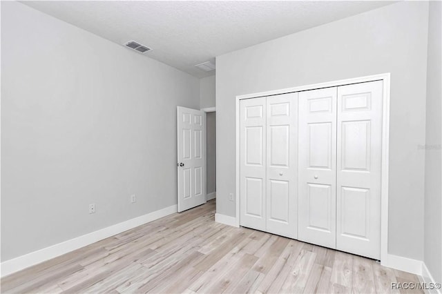 unfurnished bedroom featuring a textured ceiling, light wood-type flooring, and a closet