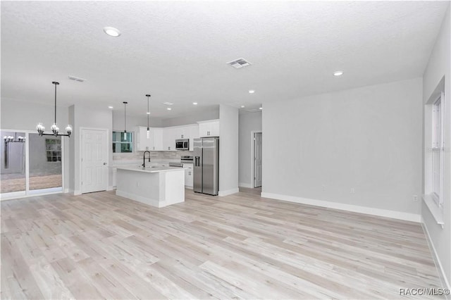 kitchen featuring sink, hanging light fixtures, stainless steel appliances, an island with sink, and white cabinets