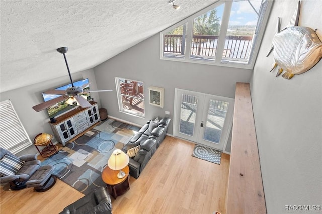 living room featuring lofted ceiling, light hardwood / wood-style flooring, ceiling fan, a textured ceiling, and french doors