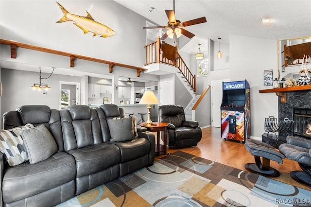 living room with ceiling fan, a stone fireplace, high vaulted ceiling, and light wood-type flooring