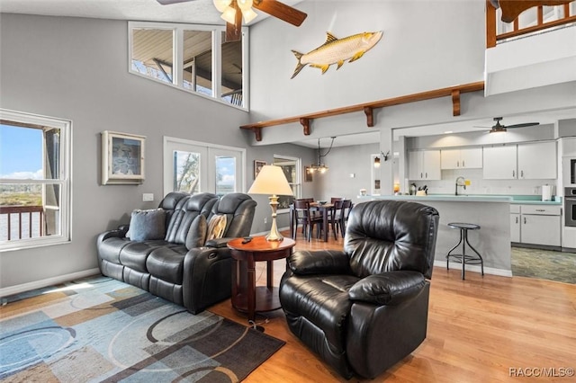 living room featuring french doors, sink, light hardwood / wood-style flooring, a towering ceiling, and ceiling fan