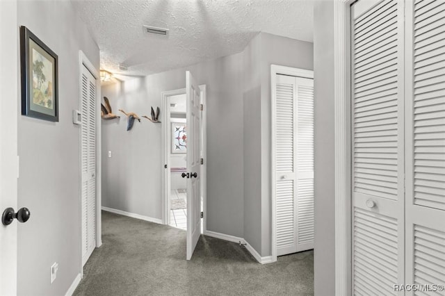 corridor featuring dark colored carpet and a textured ceiling