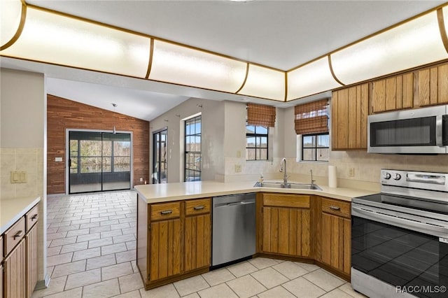 kitchen with kitchen peninsula, stainless steel appliances, vaulted ceiling, sink, and hanging light fixtures