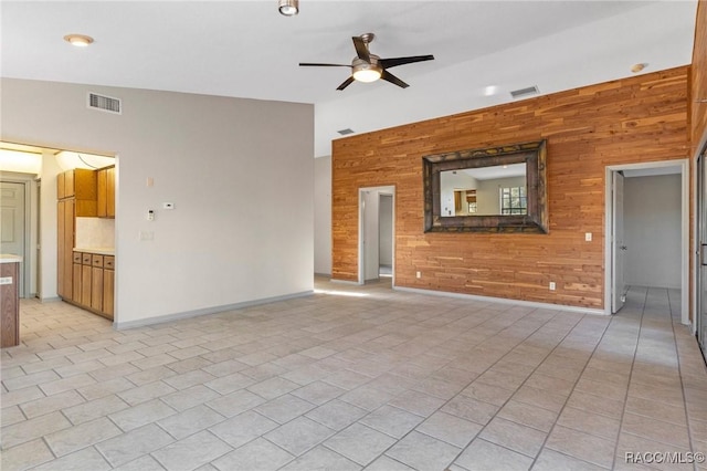 unfurnished living room featuring ceiling fan, light tile patterned floors, wooden walls, and vaulted ceiling