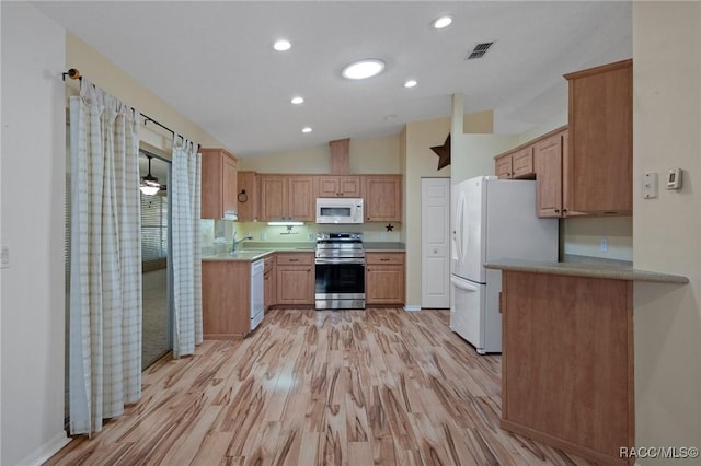 kitchen with white appliances, lofted ceiling, light countertops, light wood-style floors, and a sink