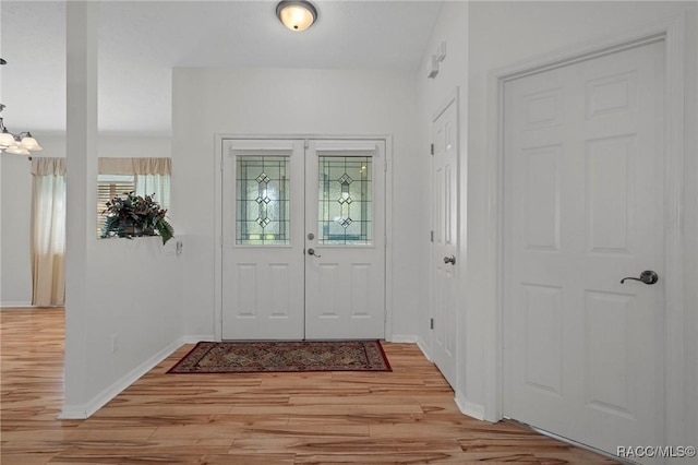 entryway with light wood-style floors, french doors, a chandelier, and baseboards