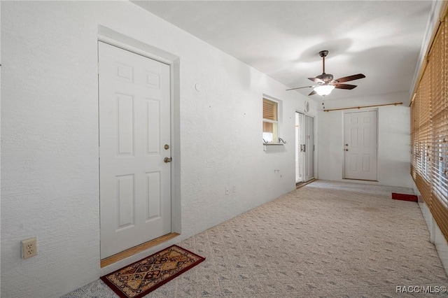 foyer entrance with carpet floors, a ceiling fan, and a textured wall