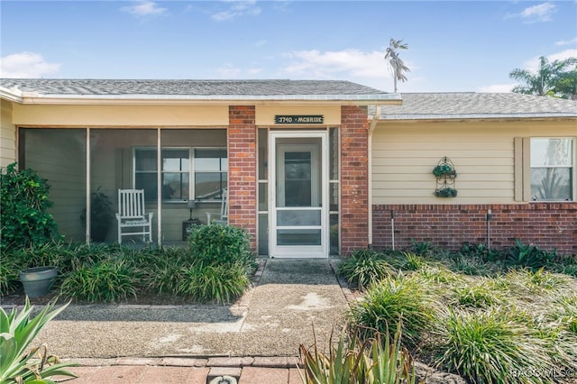 doorway to property featuring roof with shingles and brick siding