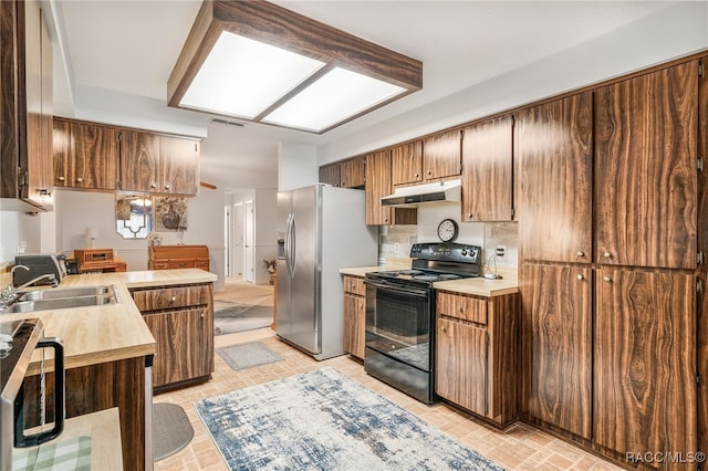 kitchen featuring under cabinet range hood, stainless steel appliances, a sink, light countertops, and decorative backsplash