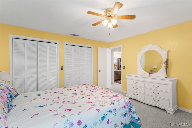 bedroom with baseboards, visible vents, a ceiling fan, light colored carpet, and multiple closets