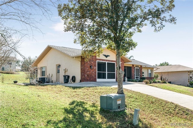 ranch-style home with driveway, central AC unit, stucco siding, a front lawn, and brick siding