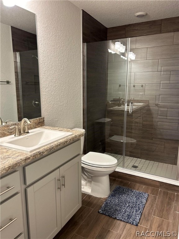 bathroom with vanity, a textured ceiling, toilet, and a shower with shower door