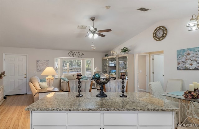 kitchen with vaulted ceiling, light stone countertops, white cabinets, and light hardwood / wood-style floors