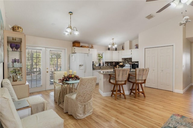 dining space featuring lofted ceiling, ceiling fan with notable chandelier, light hardwood / wood-style flooring, and french doors