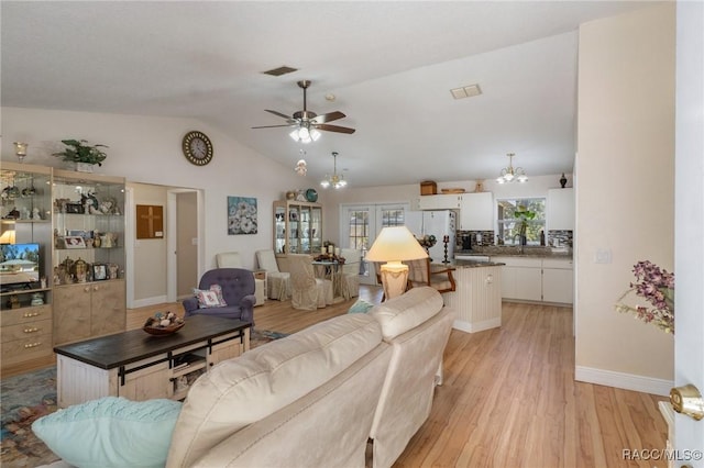 living room with ceiling fan with notable chandelier, vaulted ceiling, and light hardwood / wood-style flooring