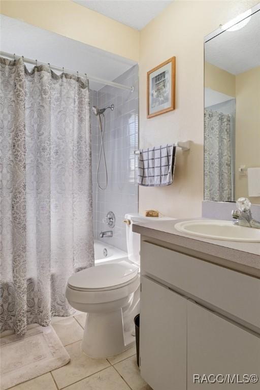 full bathroom featuring shower / bathtub combination with curtain, tile patterned floors, toilet, and vanity