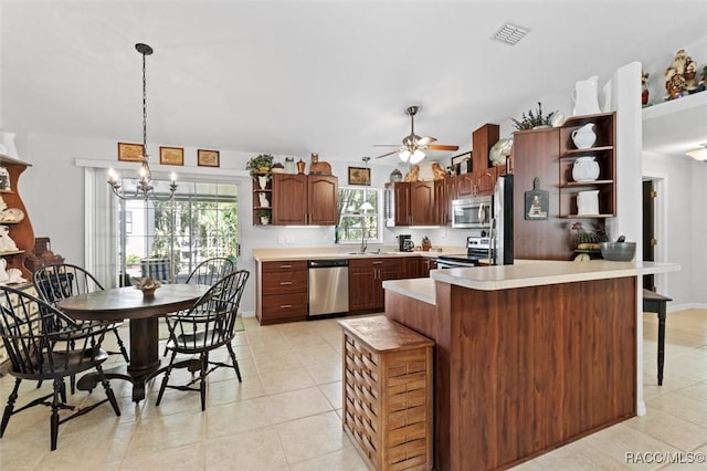 kitchen with a wealth of natural light, ceiling fan with notable chandelier, stainless steel appliances, sink, and hanging light fixtures