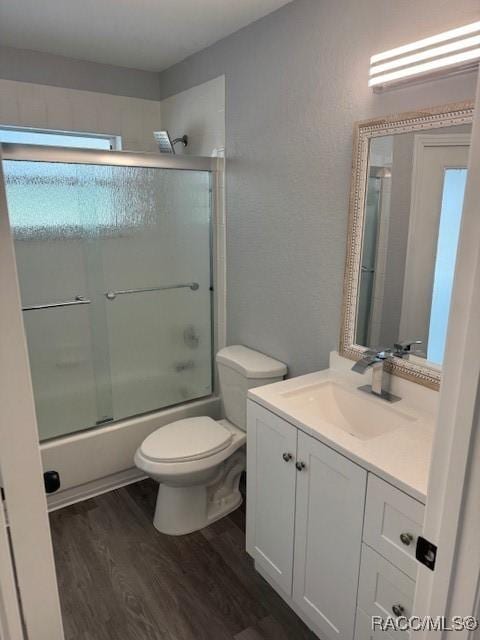 full bathroom with hardwood / wood-style flooring, vanity, toilet, and combined bath / shower with glass door