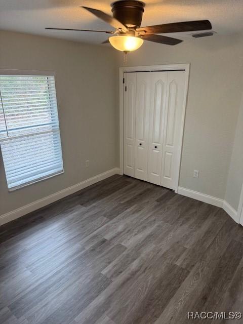 unfurnished bedroom featuring ceiling fan, dark hardwood / wood-style flooring, and a closet