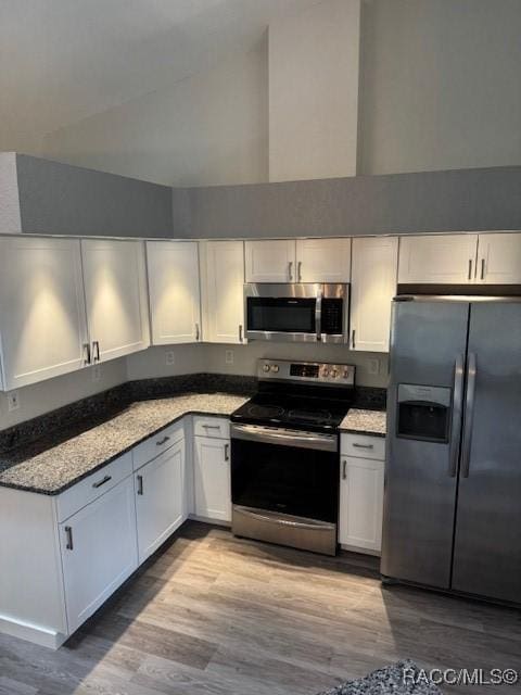 kitchen featuring white cabinetry, high vaulted ceiling, stainless steel appliances, light stone counters, and light hardwood / wood-style floors