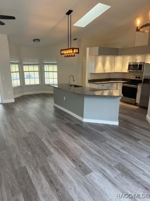 kitchen with sink, white cabinets, dark stone counters, hanging light fixtures, and stainless steel appliances