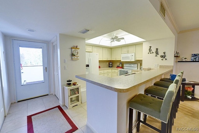 kitchen with a kitchen bar, white appliances, kitchen peninsula, and light tile patterned floors