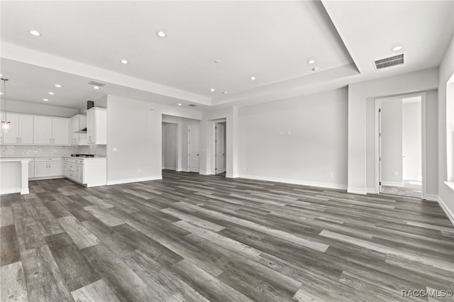 unfurnished living room featuring a raised ceiling and dark wood-type flooring