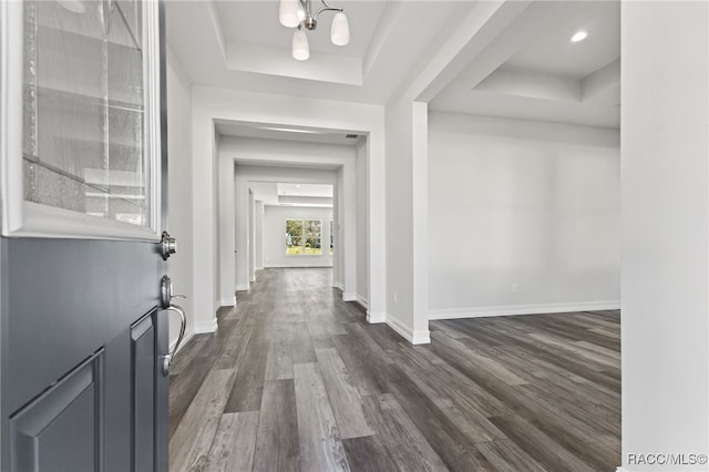 hall with dark hardwood / wood-style floors, a raised ceiling, and a chandelier