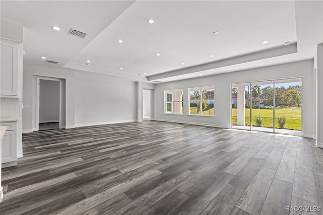 unfurnished living room featuring a raised ceiling, a healthy amount of sunlight, and dark hardwood / wood-style flooring