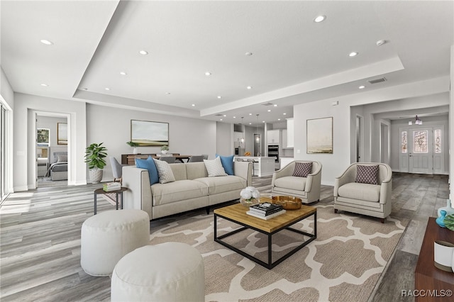 living room with light hardwood / wood-style floors and a tray ceiling