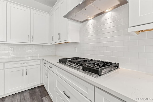 kitchen featuring decorative backsplash, wall chimney exhaust hood, dark wood-type flooring, white cabinets, and stainless steel gas stovetop