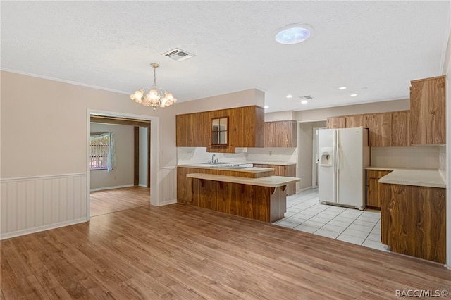 kitchen featuring kitchen peninsula, white refrigerator with ice dispenser, an inviting chandelier, light hardwood / wood-style flooring, and hanging light fixtures