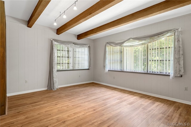 spare room featuring beamed ceiling, wooden walls, a wealth of natural light, and light hardwood / wood-style flooring