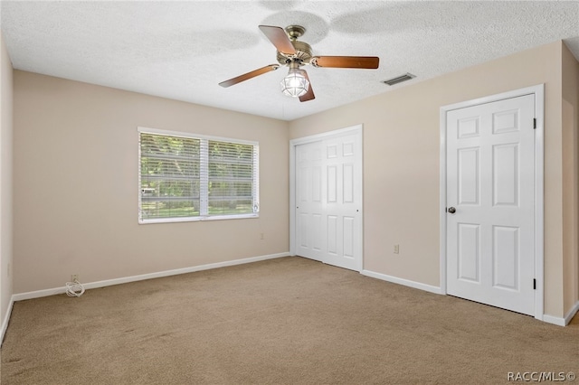 unfurnished bedroom featuring ceiling fan, light colored carpet, and a textured ceiling