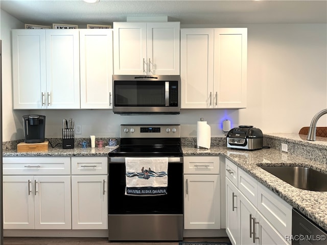 kitchen with light stone countertops, sink, white cabinets, and stainless steel appliances