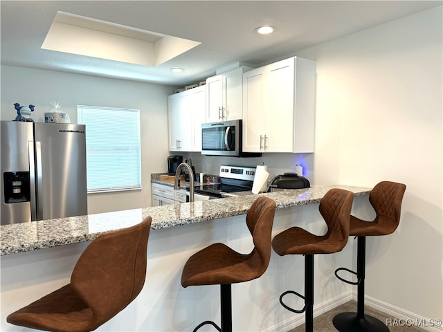 kitchen featuring a kitchen bar, light stone counters, white cabinetry, and appliances with stainless steel finishes