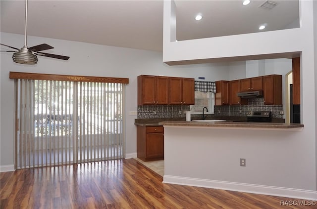 kitchen with light hardwood / wood-style flooring, ceiling fan, decorative backsplash, stainless steel range oven, and kitchen peninsula